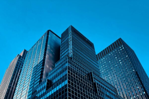 Low-angle view of modern glass office towers converging against a bright sky in cool blue corporate tones