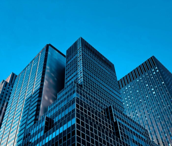 Low-angle view of modern glass office towers converging against a bright sky in cool blue corporate tones