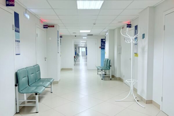 Empty modern clinic corridor with rows of benches and numbered doors in clean white and pale grey tones