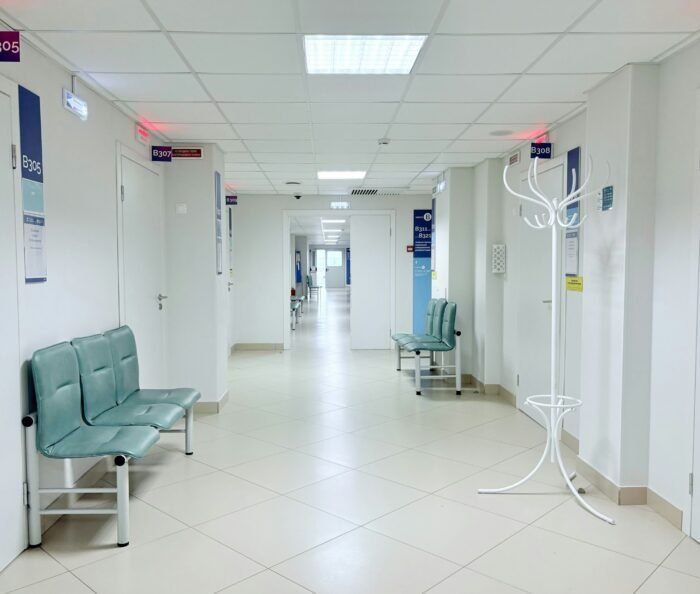 Empty modern clinic corridor with rows of benches and numbered doors in clean white and pale grey tones