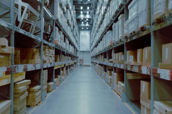 Empty warehouse aisle with tall industrial racking stacked with palletised cardboard boxes under cool blue lighting