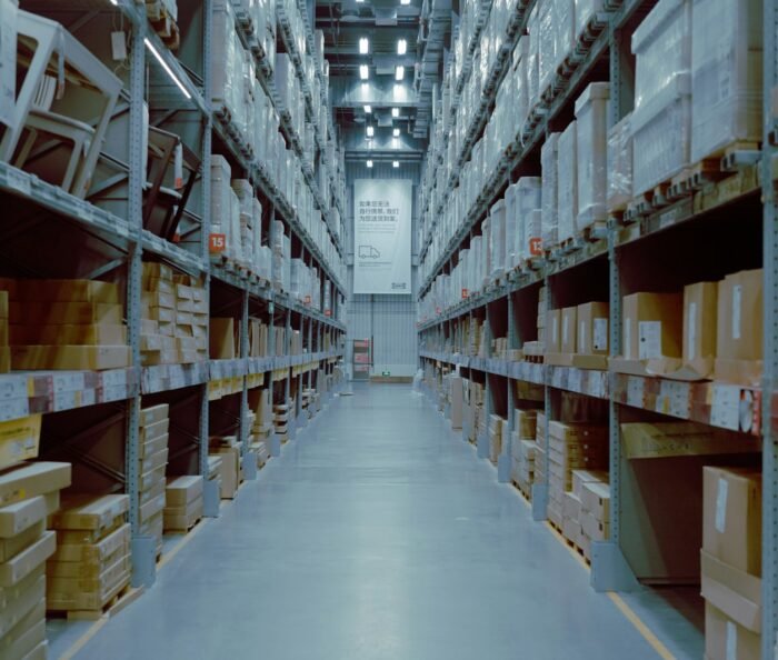 Empty warehouse aisle with tall industrial racking stacked with palletised cardboard boxes under cool blue lighting