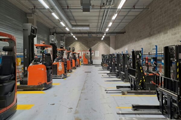 Rows of forklifts parked in an orderly grey-concrete warehouse depot, an organised industrial workplace with no people present.