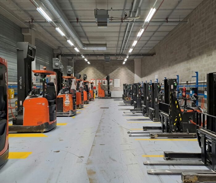 Rows of forklifts parked in an orderly grey-concrete warehouse depot, an organised industrial workplace with no people present.