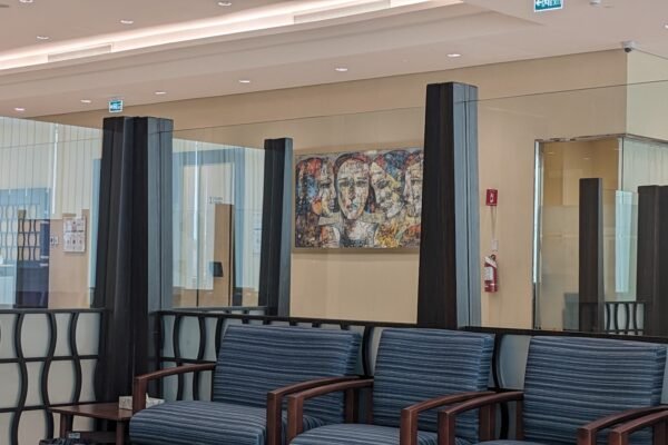 Empty modern clinic waiting area with rows of blue upholstered chairs, dark glass partitions and a framed abstract mural.