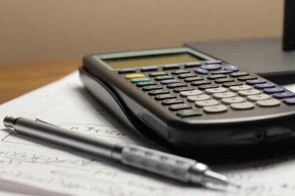 Overhead view of a calculator and a pen resting on a sheet of financial paperwork on a plain desk