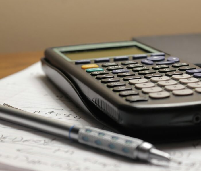 Overhead view of a calculator and a pen resting on a sheet of financial paperwork on a plain desk