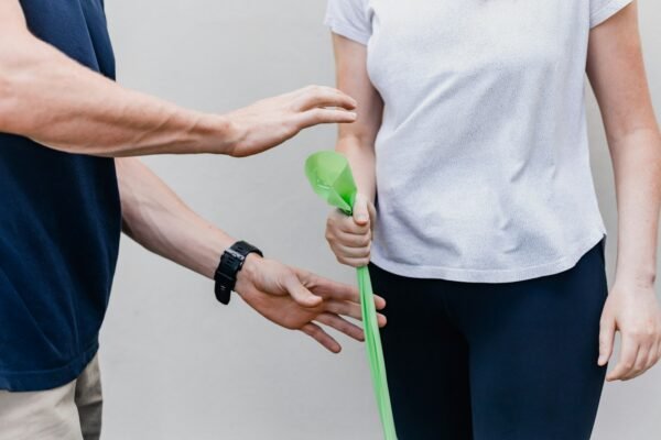 Physiotherapist guiding a client through a green resistance-band strengthening exercise, shown from the torso and hands only