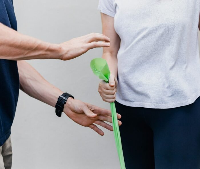Physiotherapist guiding a client through a green resistance-band strengthening exercise, shown from the torso and hands only