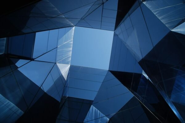 Abstract geometric mirrored-glass building facade in deep navy-blue tones, viewed from below looking upward