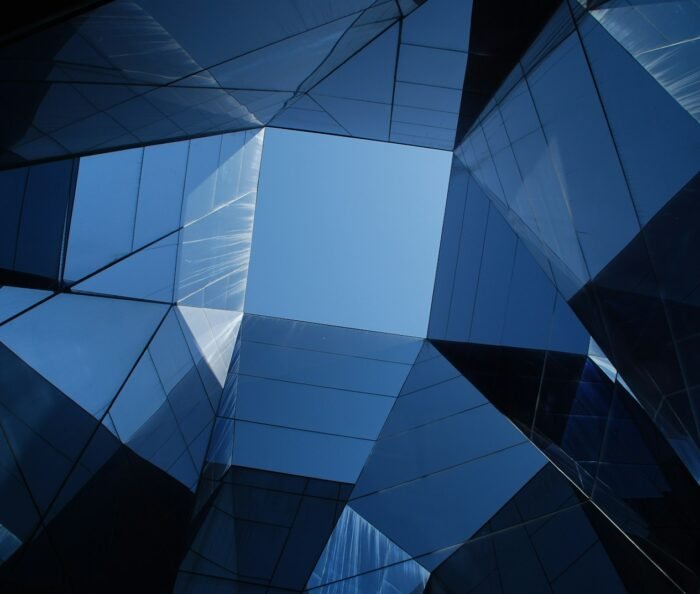 Abstract geometric mirrored-glass building facade in deep navy-blue tones, viewed from below looking upward