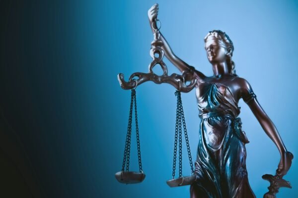 Bronze Lady Justice statue holding balanced scales against a deep blue gradient background