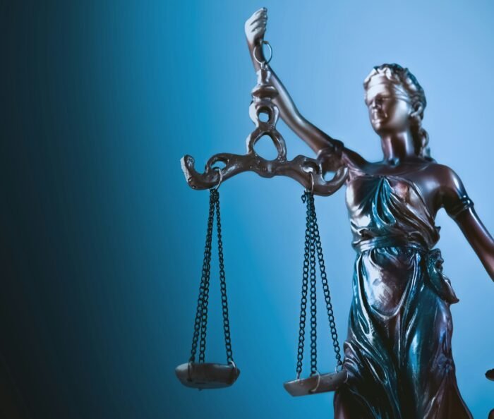 Bronze Lady Justice statue holding balanced scales against a deep blue gradient background