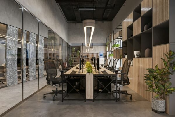 Empty open-plan office with rows of desks, ergonomic chairs and potted plants under soft overhead lighting