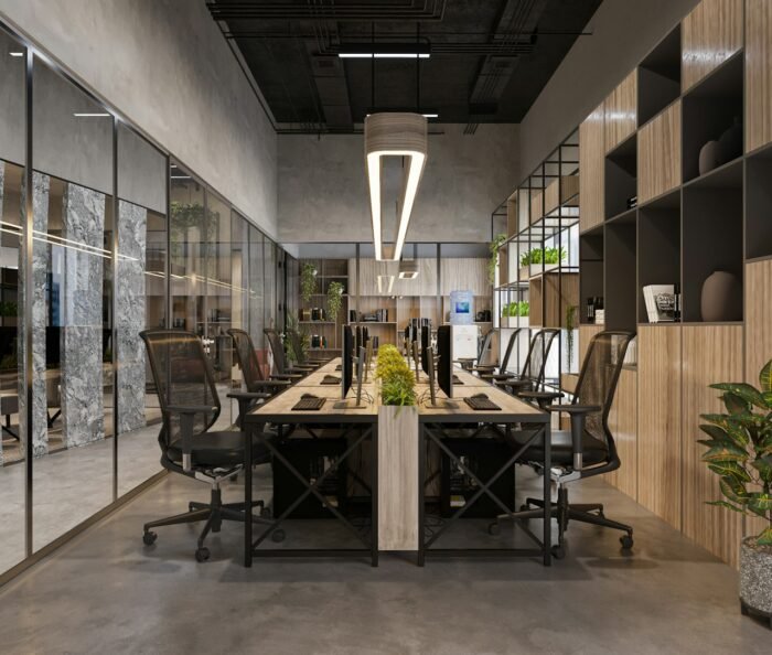 Empty open-plan office with rows of desks, ergonomic chairs and potted plants under soft overhead lighting