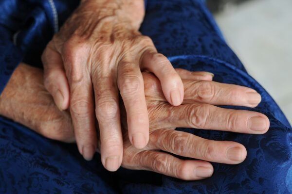 Elderly person's clasped, weathered hands resting gently on deep navy-blue fabric