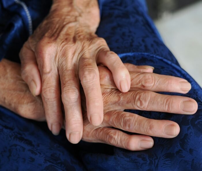 Elderly person's clasped, weathered hands resting gently on deep navy-blue fabric