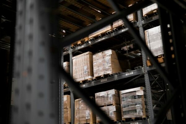 Tall steel pallet racking stacked with shrink-wrapped palletised boxes inside a dim industrial warehouse