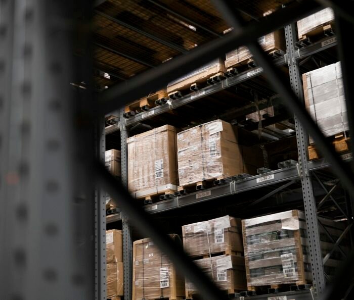 Tall steel pallet racking stacked with shrink-wrapped palletised boxes inside a dim industrial warehouse