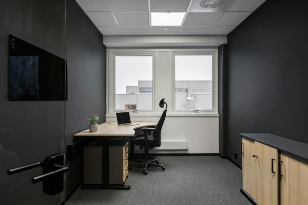 Empty modern office consultation room with desk, ergonomic chair and daylight window, no staff present