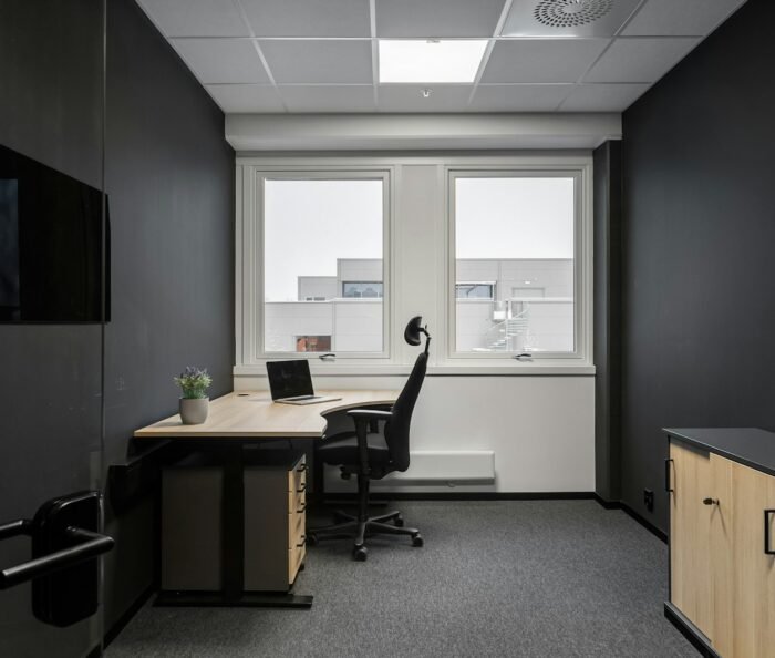 Empty modern office consultation room with desk, ergonomic chair and daylight window, no staff present