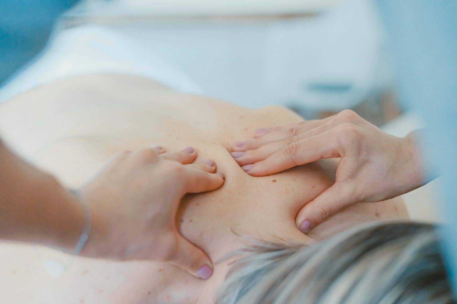 Therapist's hands performing a shoulder and upper-back treatment on a patient lying on a treatment table