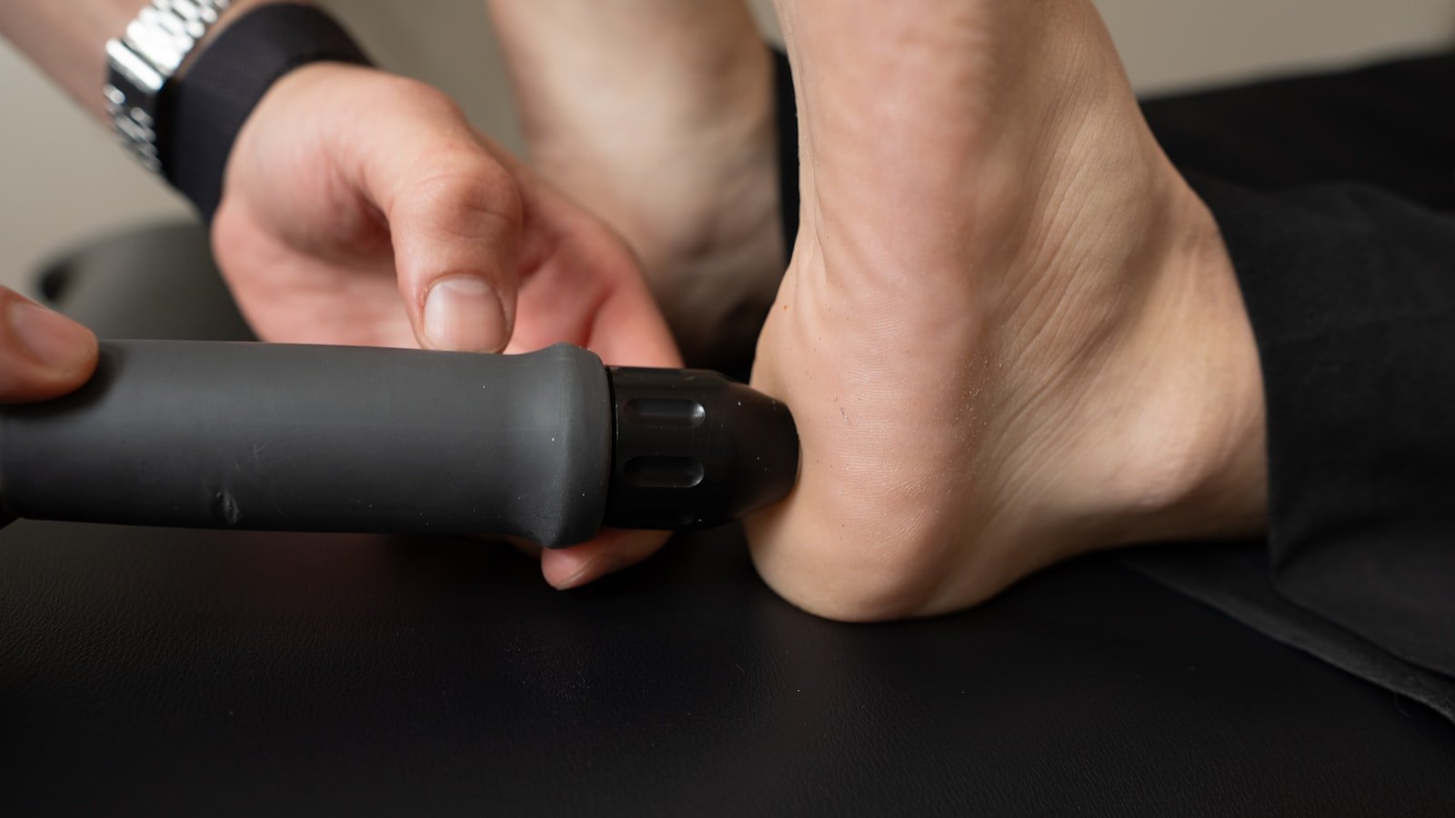 Close-up of a clinician's hands applying shockwave therapy to a patient's heel on a treatment table