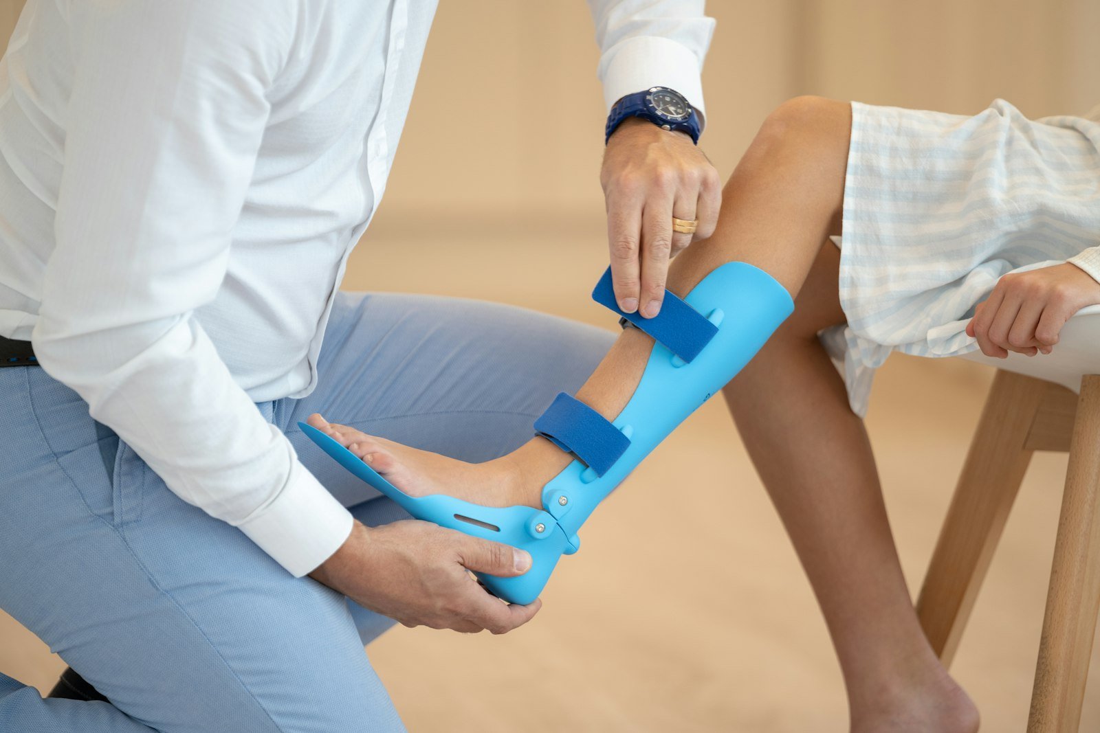 Clinician's hands fitting a blue ankle-foot brace on a patient's lower leg