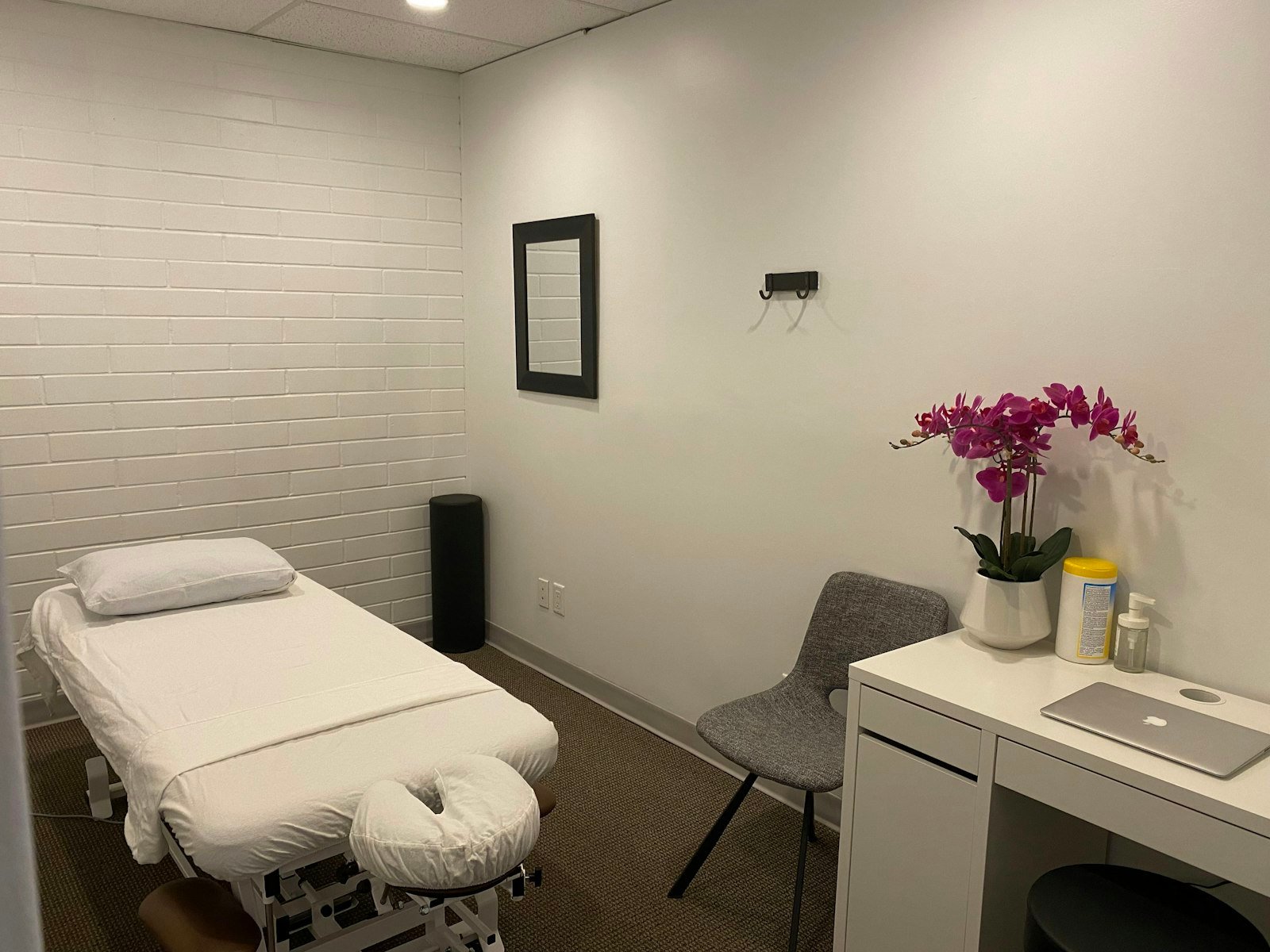 Clean treatment room with a padded therapy table, consult chair and small desk