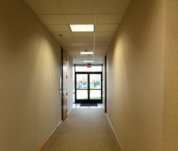 Empty, quiet office corridor with a closed door, evoking the isolation of a workplace psychological injury.